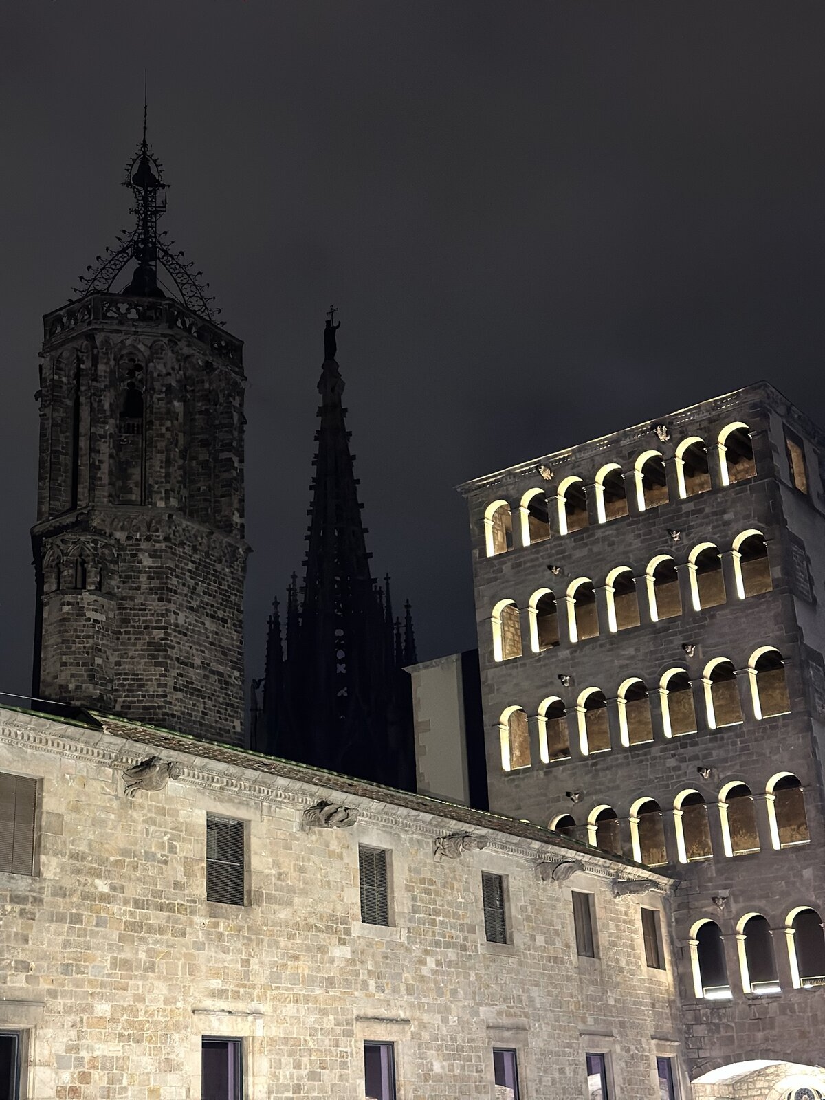 Gothic cathedral towers lit up against the night sky in Barcelona's old quarter.
