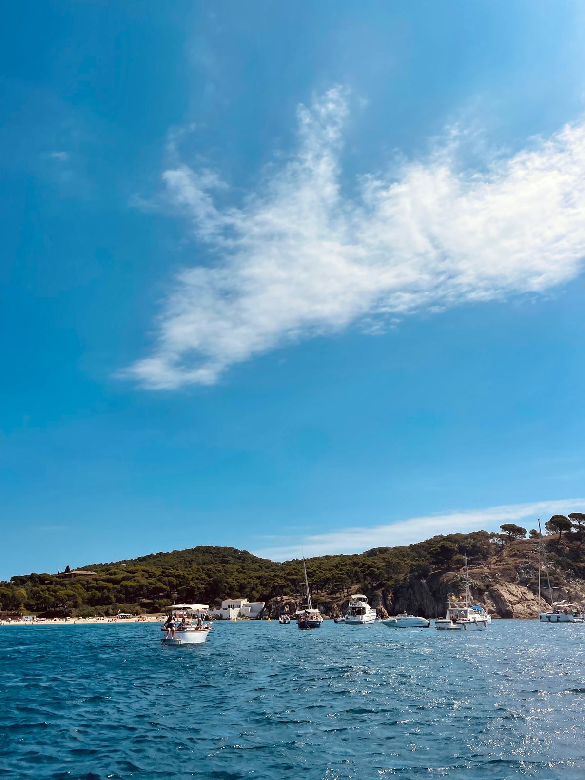 A wide bay dotted with small boats, hillside village rising behind the water.