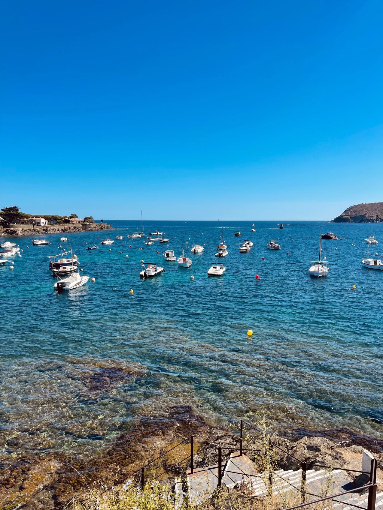 A turquoise bay with small boats anchored near a Costa Brava village on the shore.