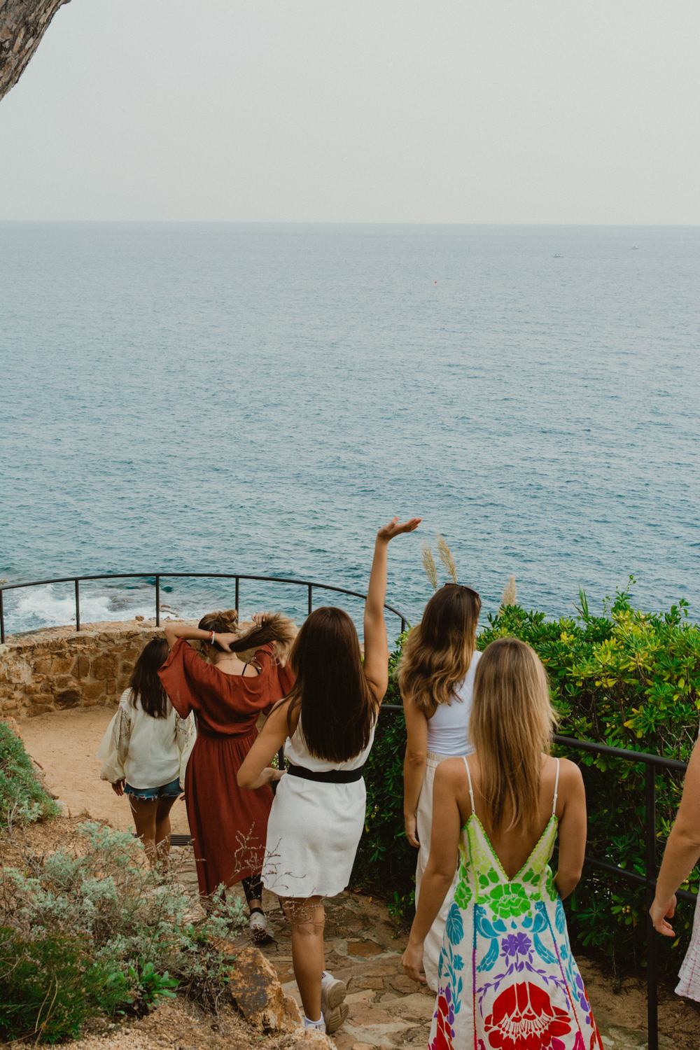 A group of women, backs to the camera, descending stone stairs toward a cliff overlook.