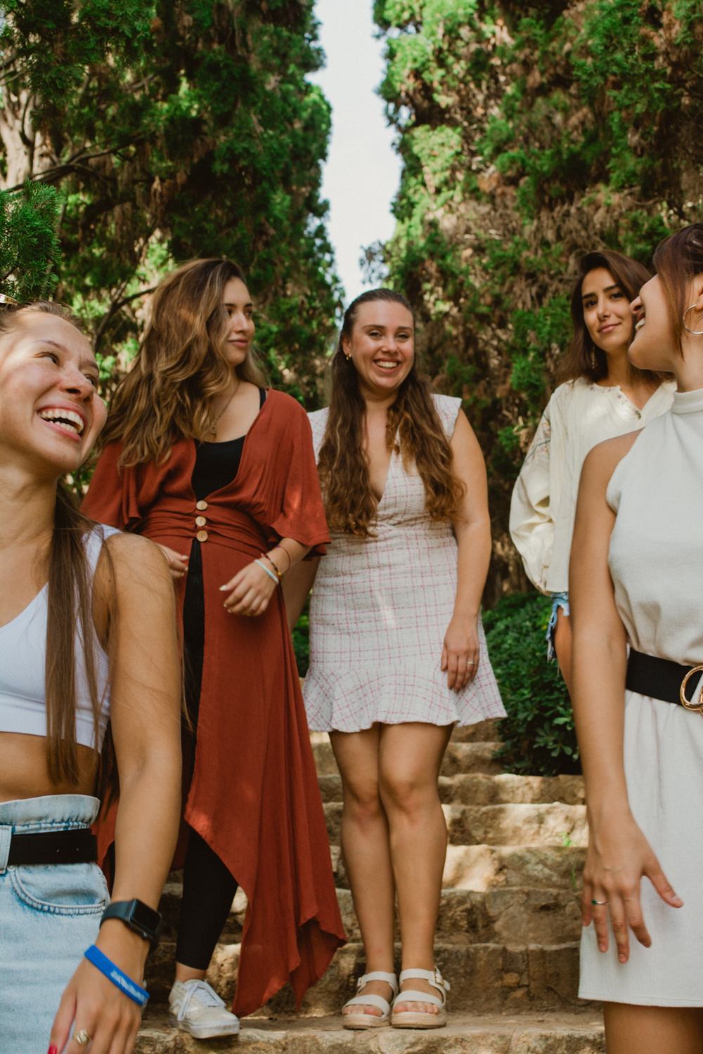 A group of women laughing together while walking down a shaded alley lined with tall cypress trees.