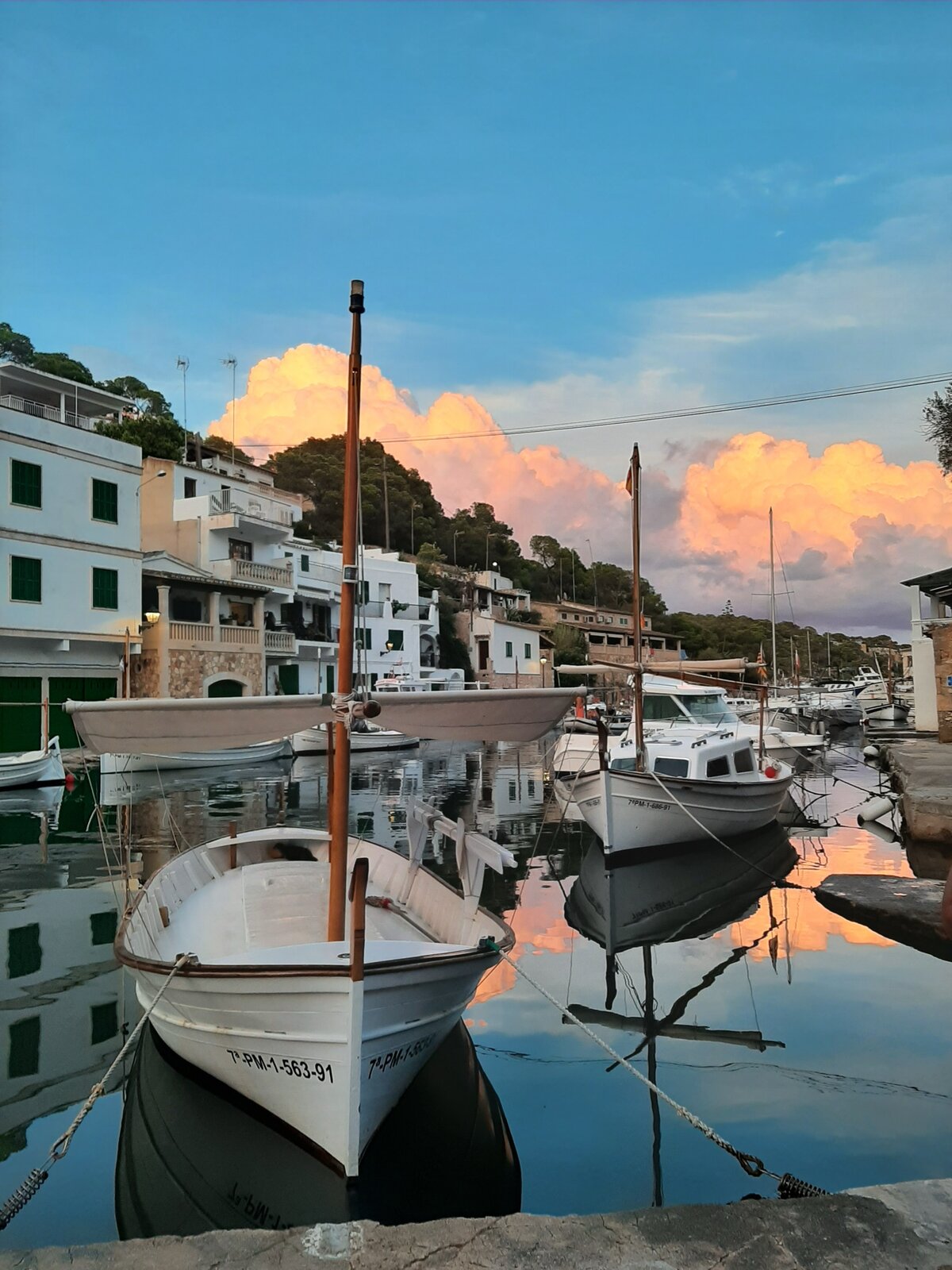 Small fishing boats reflected in the still water of a Catalan harbor at sunset.