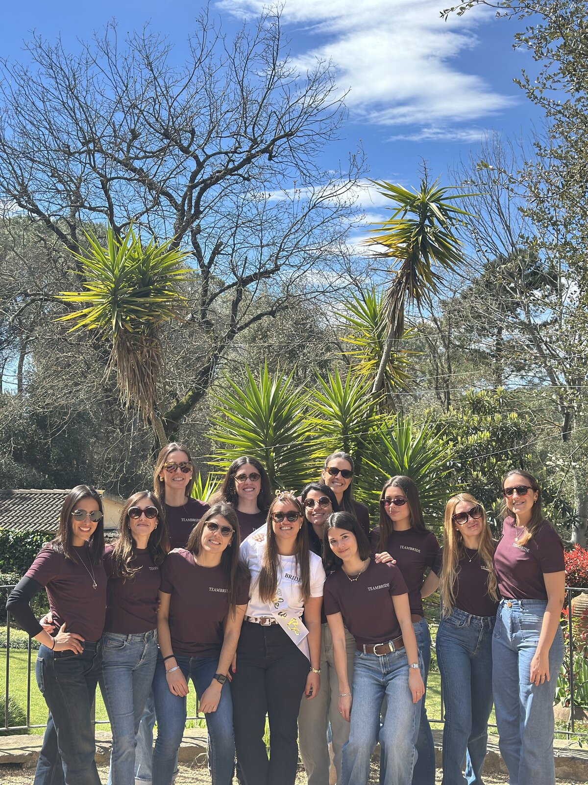 A group of women in matching burgundy shirts posing together outdoors for a team retreat.