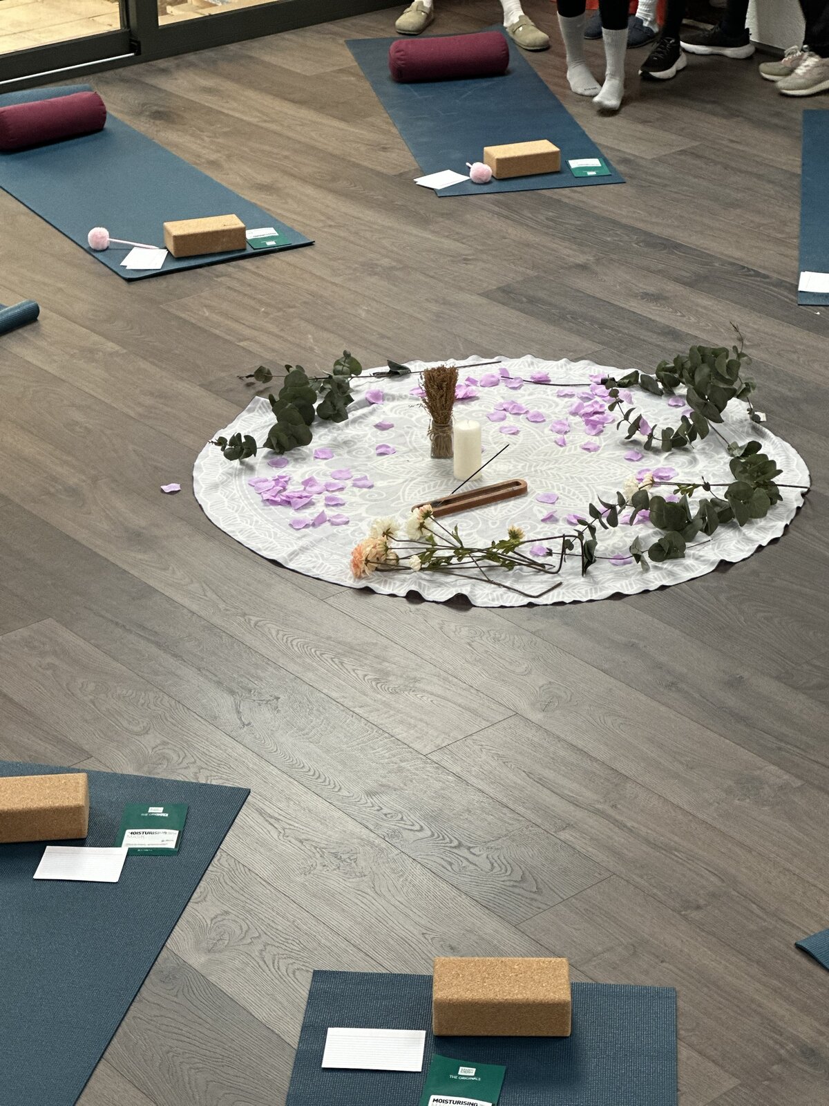 A yoga studio floor set with mats, bolsters, and a small flower altar.